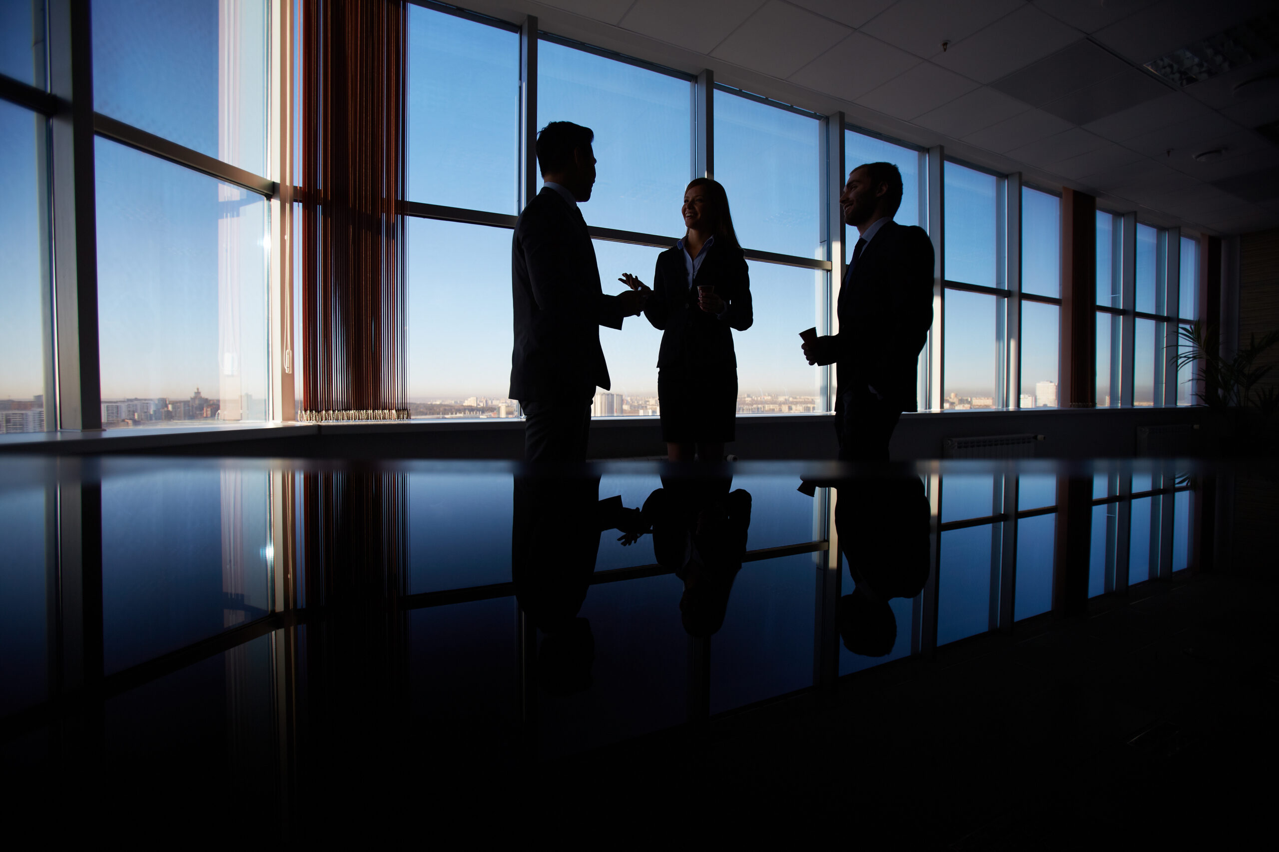 Outlines of three office workers interacting by the window